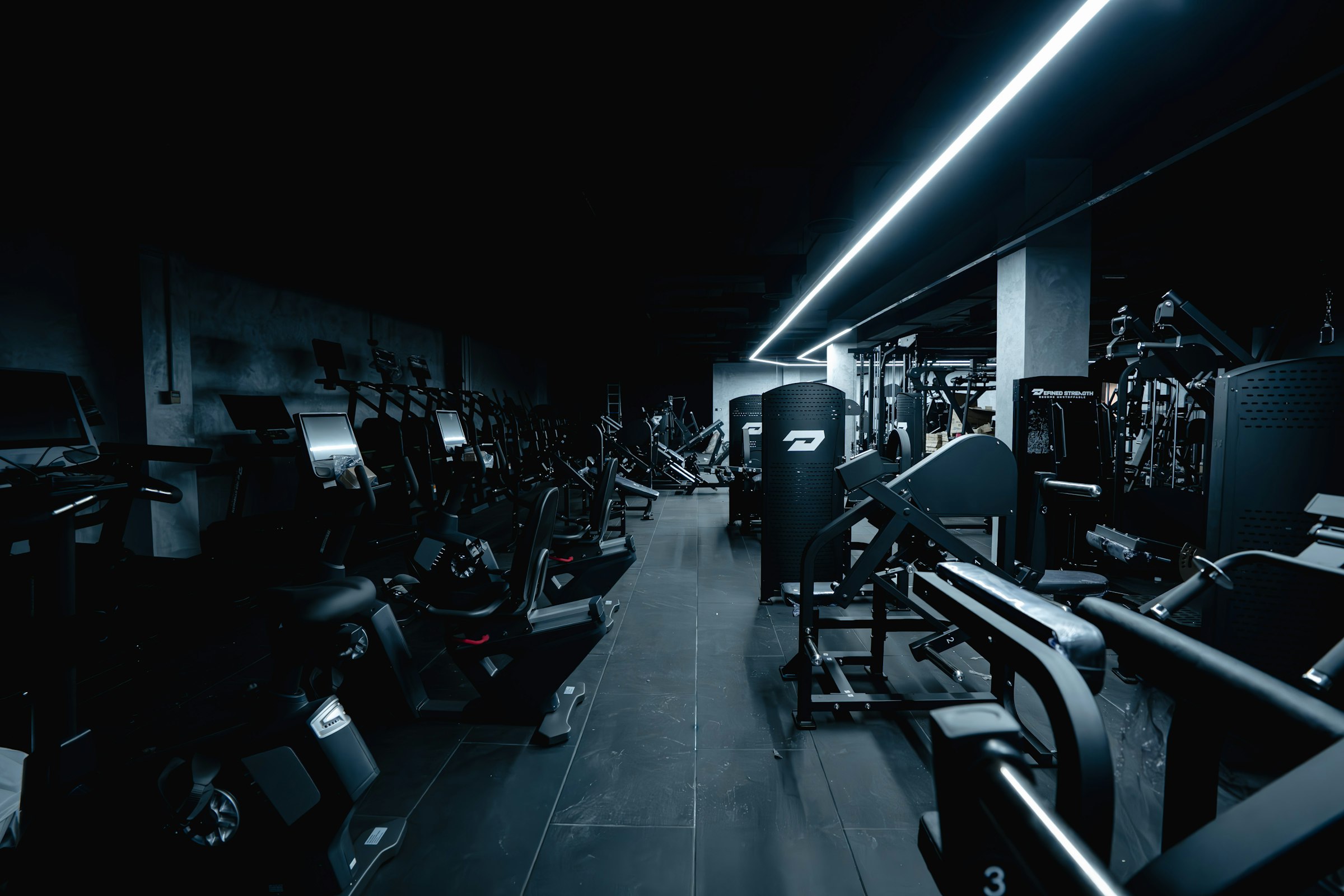 Rows of weight machines in a dimly lit gym with a single strip of light